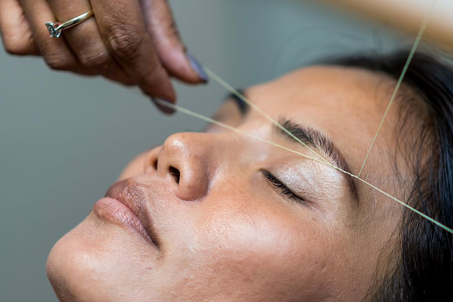 a woman removes her eyebrows hair by threading method