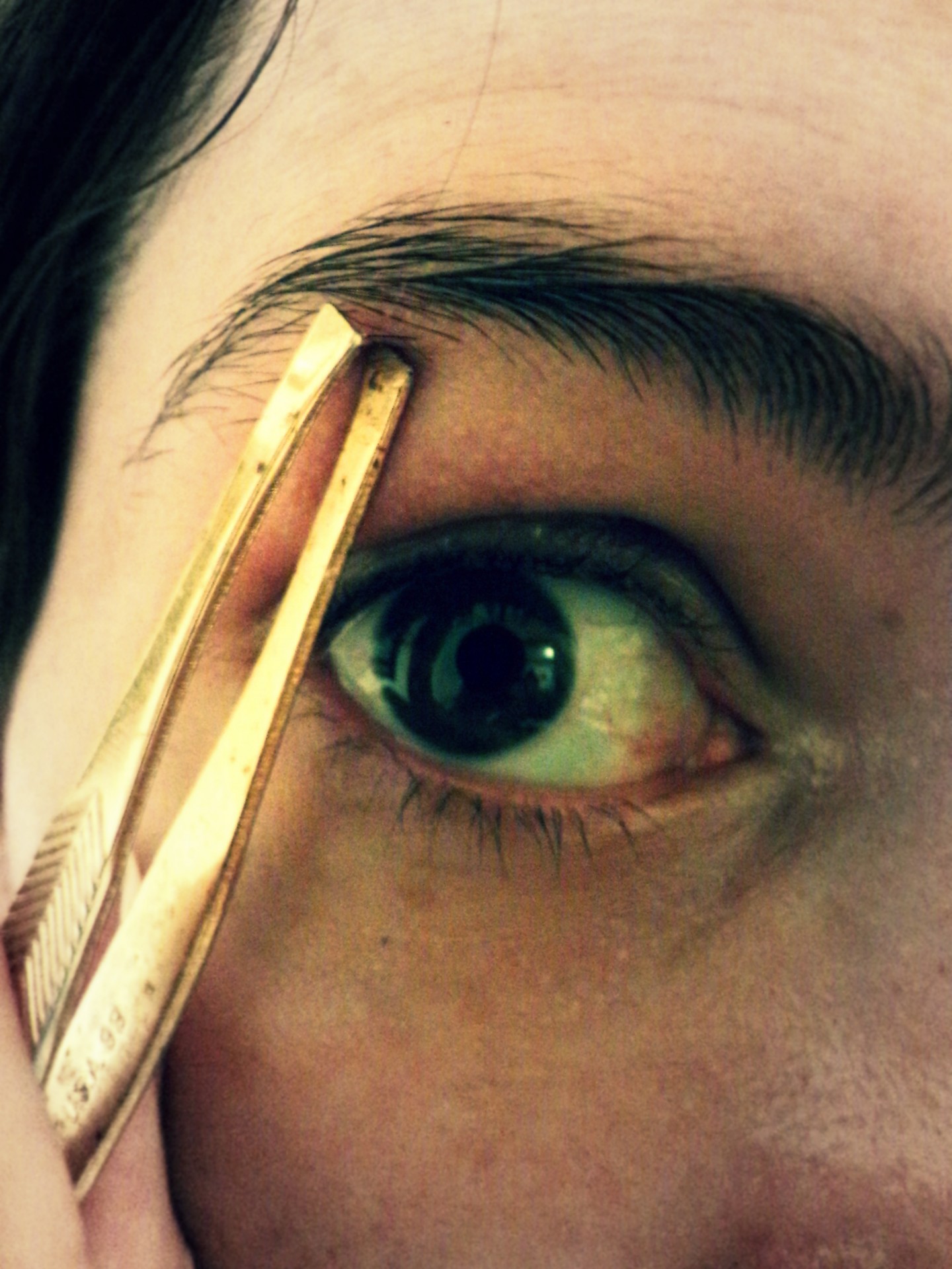 a woman uses a tweezer to remove unwanted hair from eyebrows