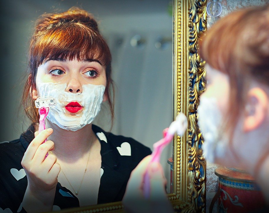 a woman shaving her face with a razor