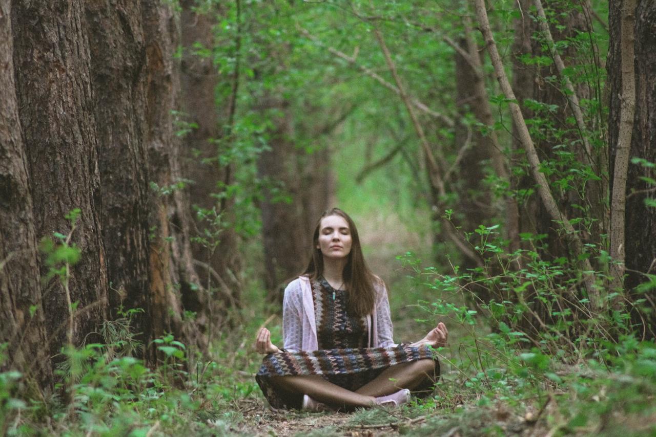 a woman is sitting in the jungle doing meditation